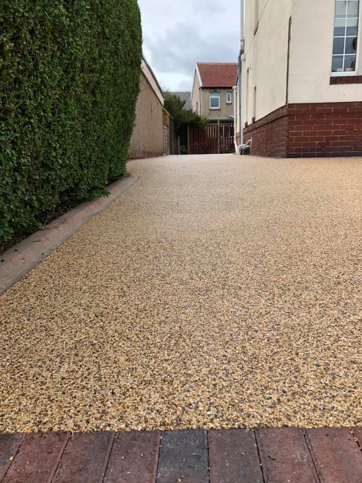 Long golden resin driveway beside a hedge