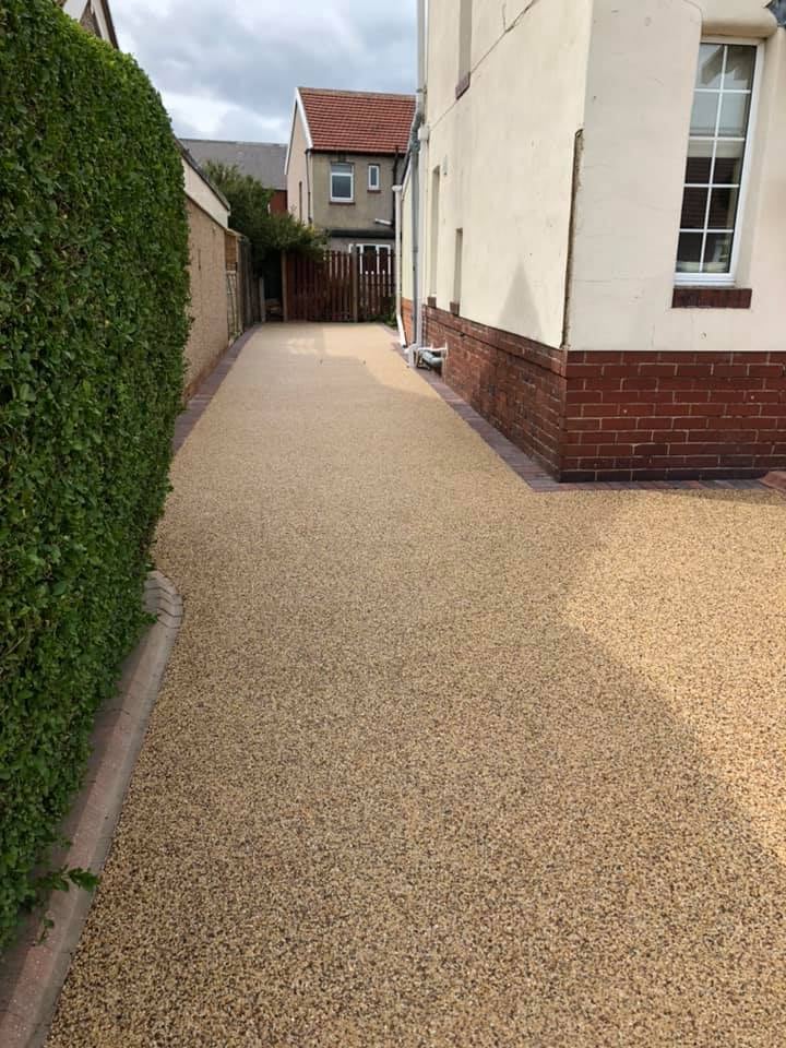 Long golden resin driveway running beside a hedge